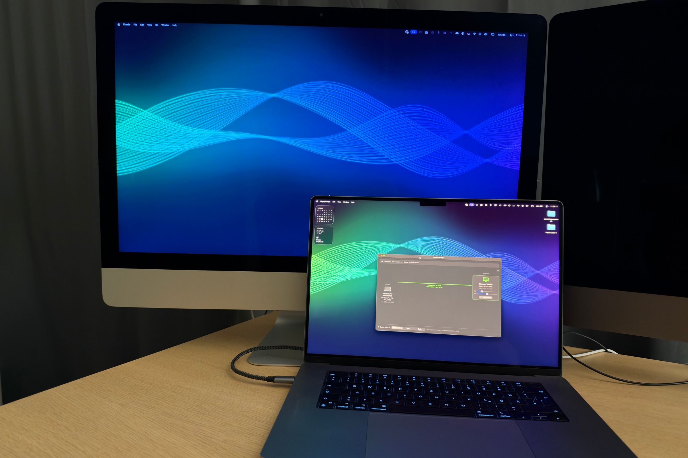 Un iMac de 27 pulgadas con un fondo de ondas azules como segunda pantalla del MacBook Pro que tiene delante, que muestra la ventana de DisplayBridge; un solo cable los conecta.