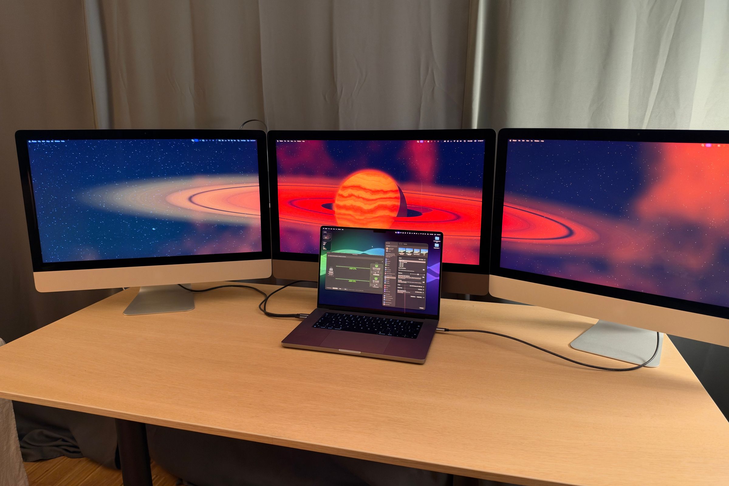 Tres iMac de 27 pulgadas uno al lado del otro en un escritorio, con un fondo de un planeta con anillos, y delante un MacBook Pro conectado por cable que muestra la ventana de DisplayBridge.