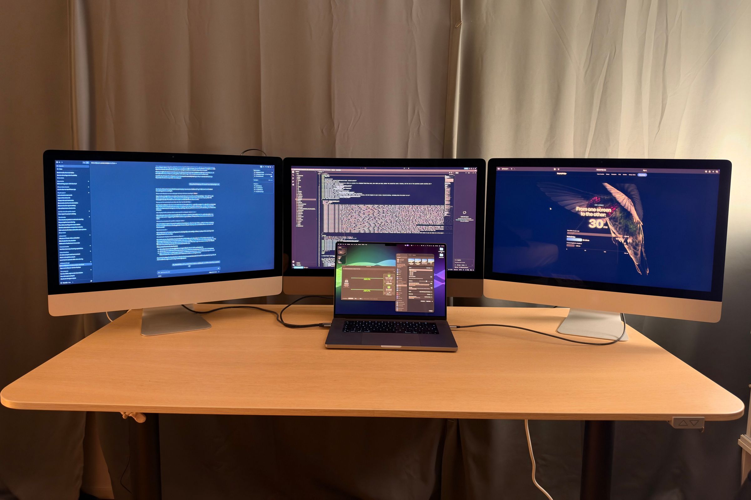 Tres iMac usados como pantallas de un MacBook Pro: documentos a la izquierda, un editor de código en el centro y una web a la derecha, con el MacBook delante.