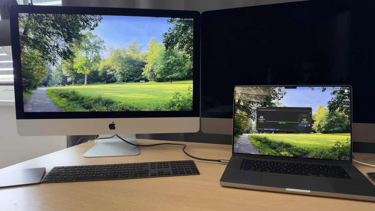 An iMac next to a MacBook Pro, showing the MacBook's second desktop